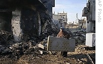 A Palestinian woman carries a mattress from the rubble of a building in an area targeted by Israeli air strikes in Rafah, southern Gaza Strip, Monday, 12 Jan. 2009