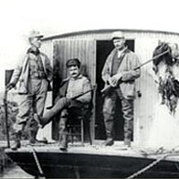 Capt. J.W. Quillen on his shantyboat with two hunters, c. 1920
