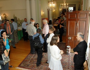 Photo of the Stone House foyer during Fogarty's birthday celebration in July. View looking down from the staircase shows people standing around talking.