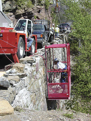 Many retaining walls, like this one near Crystal Point, are being "repointed," the process of removing and replacing damaged and deteriorated mortar. Here a crane lowers a worker, enclosed for safety in a cage-like basket, to perform repairs.