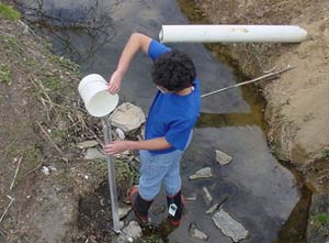 Student gathering water from a creek to check turbidity