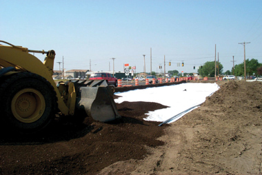 Photo: A tractor begins placing a 30.5 centimeter (12-inch) blended base on a subgrade fabric reinforcement prior to compaction activities during a paving project on State Street in Bismarck, ND.