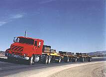 Load is applied to test sections of WesTrack with four identical triple-trailer trucks, each of which is loaded with tied-down steel plates totaling a weight of 676 kilonewtons.