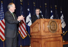 Evans applauding Gutierrez on stage with U.S. and Commerce flags in background. Click for larger image.