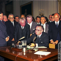 Johnson at desk signs Civil Rights Act of 1964, congressional leaders and attorney general behind him (AP Images)