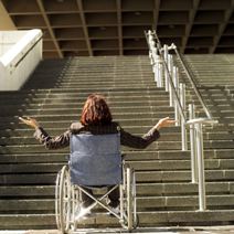 Woman in wheelchair looks up at a long stairway entrance.