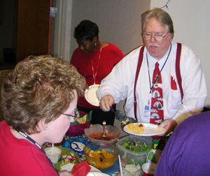 Sporting his holiday tie, Phil Hanson, right, built his plate, as Donna Byrd, foreground, tried to decide where to begin. Celeste Edwards wass in the background making difficult choices from among the abundance of goodies.