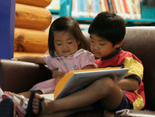 a photo of two preschool-age children looking at a book. 