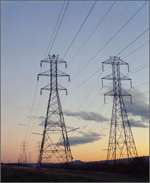 A photo at sunset of tall electricity transmission towers connected for miles by transmission wires. 