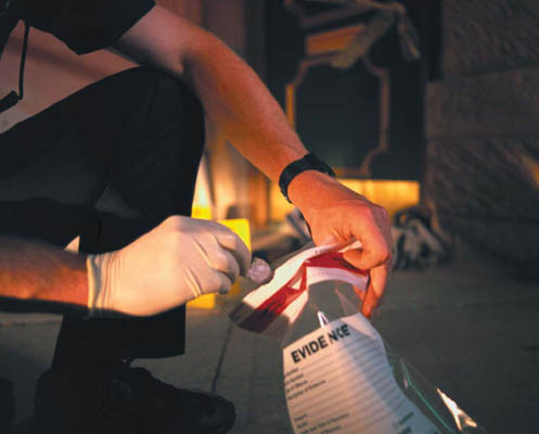 Photograph of police officer placing an item into evidence collection bag at a crime scene