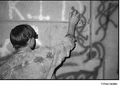 Photograph of a young man spray painting graffiti on a wall