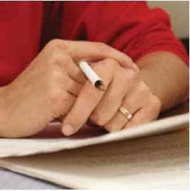 Photograph of two hands (one holding a pen) resting on some papers