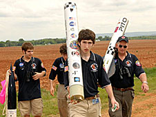 Team members holding large sections of a rocket