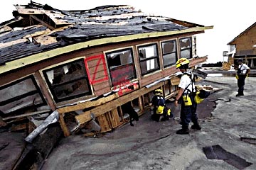 Photo of a firefighter standing in front of a house damaged by a fire.