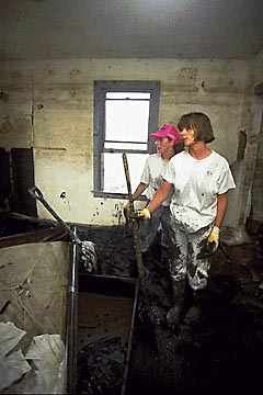 Photo of two people looking at the damage to a house.