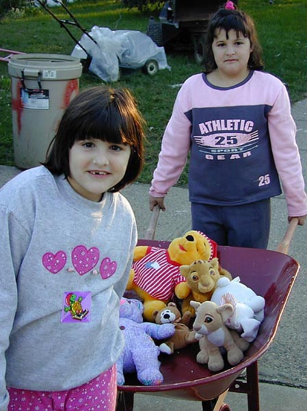 Photo of two children carrying their toys in a wheel barrow.