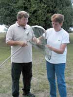 Picture of a man holding a net with a woman reaching for the captured monarch inside the net.