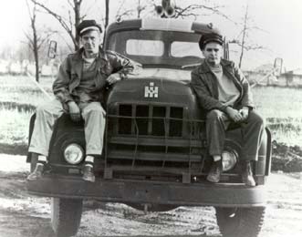 picture of 2 men in leather jackets sitting on the hood of a bobtail tractor