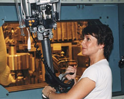 An operator protected by a shielded window using robotics in a “hot cell” at a radioactive handling facility.