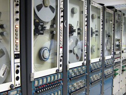 The machines pictured read the inch-wide magnetic data tape from their 14-inch reels. Multiple machines are used because each reel only records about 15 minutes worth of data. As one reel fills, the next machine automatically starts recording a slight overlap for data continuity.