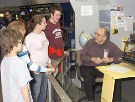 Image of a Glenn volunteer explaining an exhibit to a group of students.