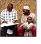 Link to Health Systems (Photo of a health worker taking information from a father and son)