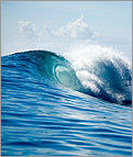 Photo of a crashing wave with sky and clouds in background.