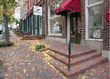 Case Study: Photo shows sloping street with brick sidewalks serving shop entrances.  Level runouts on the high side of the approach are used to provide accessible routes to the entrance doors, while steps connect entrance platforms from the low side.