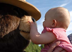 A baby grabbing and examining the nose of Smokey Bear.