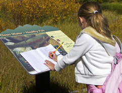 A young female student examining a Clean Water sign and is taking notes in her workbook. 