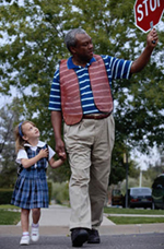 Image of a crossing guard helping a young girl cross the street.
