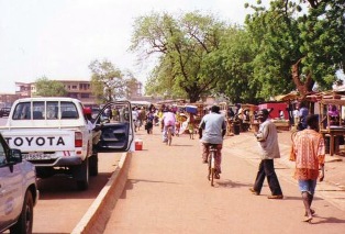 Photo of Toyota truck with people walking and riding bicycles on the side of the road in Tamale, Ghana.