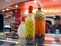 Photo of jars holding pickled vegetables in front of deli cases.