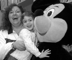 Photo: A child enrolled in a NIAMS study gives Mickey Mouse a big hug in the Children's Inn library.