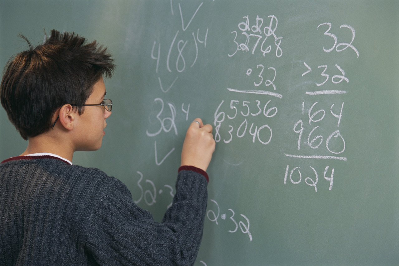Child writing mathematical equations on chalkboard