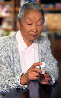 Older Asian woman reading a bottle of pills