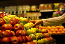 A photo of a hand picking up an apple at the supermarket.