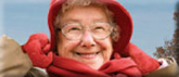 A smiling elderly woman wearing a hat, scarf, and gloves