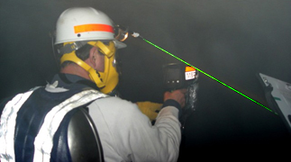 Mine rescue team captain exploring in smoke during training using a thermal imaging camera to look for missing miners and wearing a green laser to help with guidance.