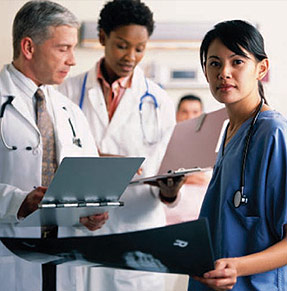 Caucasian male doctor, Black female doctor, and Asian nurse: Doctors consult with each other on medical charts, while nearby nurse holds x-ray and faces reader.
