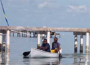 Boys maneuver boat past pier and toward beach of Caye Caulker, Belize. December 28, 2005. [&#169; AP Images]