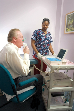 Photograph showing spirometry. The patient takes a deep breath and then blows hard into a tube connected to a spirometer. The spirometer measures the amount of air exhaled and how fast it was blown out.