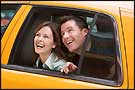 A man and a woman look excitedly out the window of a taxicab
