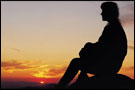 A pensive person sits silhouetted against a sunset