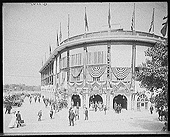 Docenas de hombres y mujeres se dirigen al Forbes Stadium. Hacia la derecha hay algunos autos aparcados. Banco y negro, c1910.