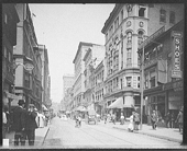 Numerosos hombres y mujeres van a sus trabajos en una calle transitada en c1906 Providence, Rhode Island. Se pueden ver diversos edificios y un carruaje tirado por un caballo en segundo plano.