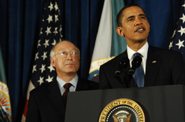 Secretary Salazar standing beside President Obama while Obama speaks to employees
