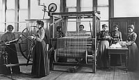 Several women with a spinning wheel and a large loom.