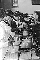 Several women at a long table, cooking on portable burners.