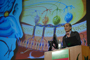 a photo of Dr. Richard Axel speaking at a podium with illustrations on a screen behind him.